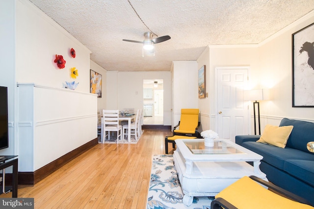 living room featuring ceiling fan, crown molding, a textured ceiling, and light wood-type flooring