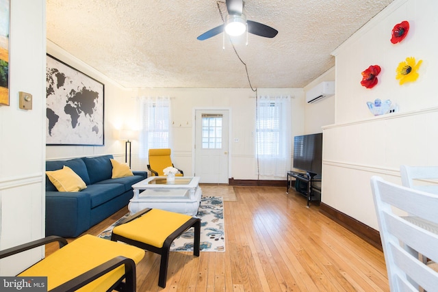 living room with ceiling fan, ornamental molding, light wood-type flooring, a textured ceiling, and a wall mounted AC