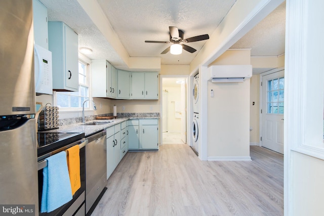 kitchen with stacked washer and clothes dryer, an AC wall unit, sink, appliances with stainless steel finishes, and light hardwood / wood-style floors