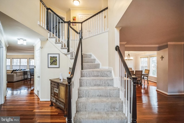 stairs featuring hardwood / wood-style flooring, ornamental molding, a high ceiling, and a notable chandelier