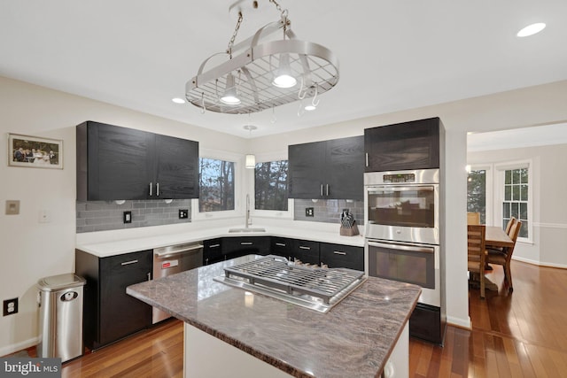 kitchen with stainless steel appliances, wood-type flooring, a kitchen island, and sink