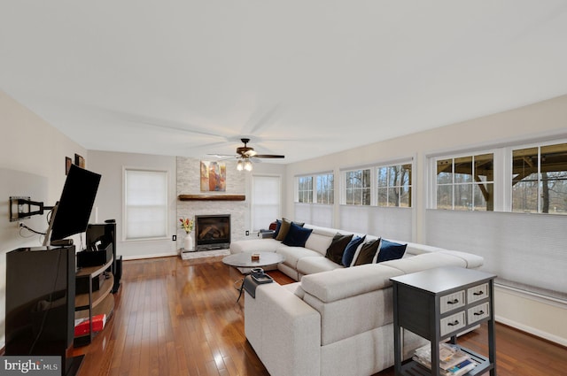 living room featuring a stone fireplace, dark wood-type flooring, and ceiling fan