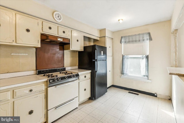 kitchen featuring black refrigerator, cream cabinetry, and white gas range oven