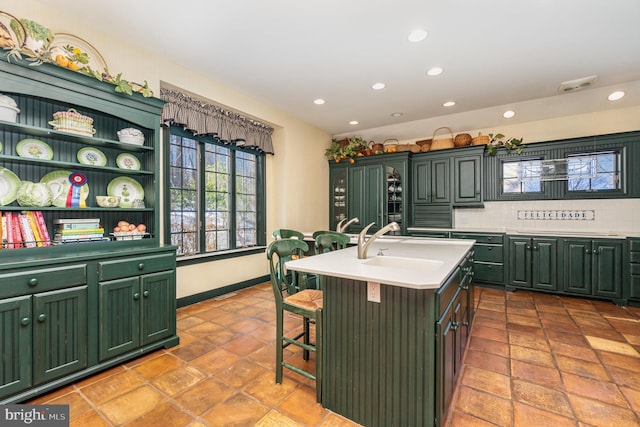 kitchen with a kitchen breakfast bar, tasteful backsplash, a kitchen island with sink, and green cabinetry