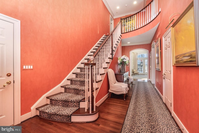 stairway featuring wood-type flooring, a towering ceiling, and crown molding