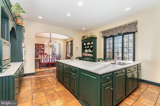 kitchen featuring a kitchen island with sink, sink, an inviting chandelier, green cabinetry, and stainless steel microwave