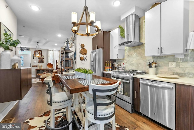 kitchen featuring white cabinets, wall chimney exhaust hood, decorative light fixtures, and appliances with stainless steel finishes