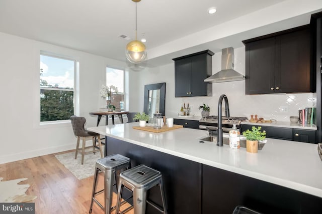 kitchen with backsplash, hanging light fixtures, wall chimney exhaust hood, light hardwood / wood-style floors, and a kitchen bar