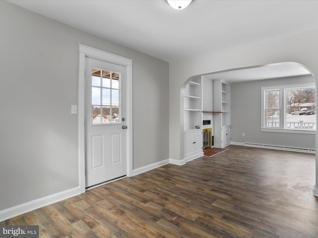 unfurnished living room featuring built in shelves, dark hardwood / wood-style floors, and a baseboard heating unit