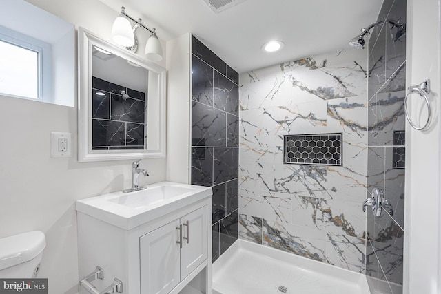 bathroom with tiled shower, vanity, and toilet