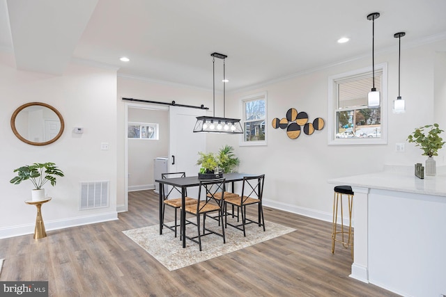 dining area with a barn door, crown molding, and dark wood-type flooring