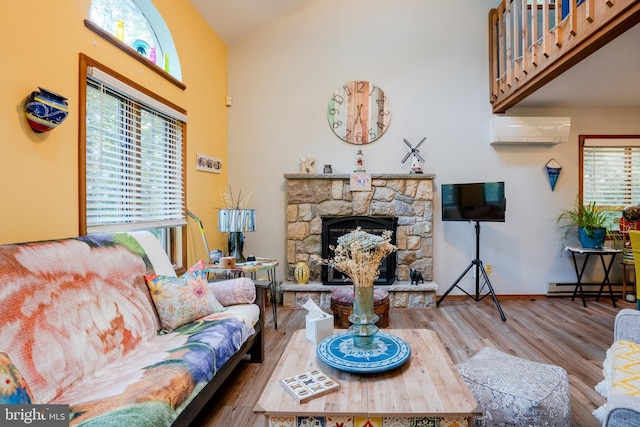 living room with a wall mounted air conditioner, lofted ceiling, a stone fireplace, a baseboard radiator, and wood-type flooring