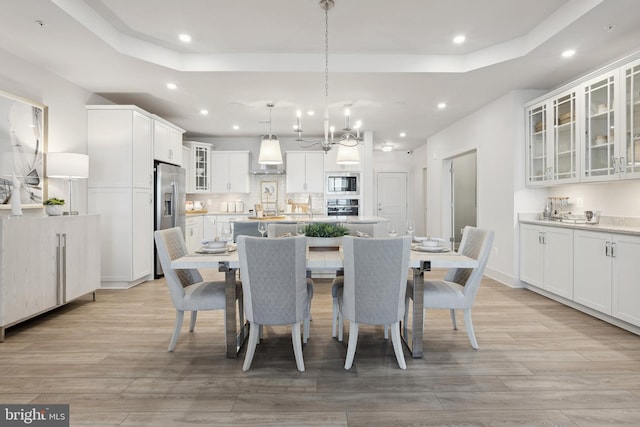 dining room featuring light wood-type flooring, a tray ceiling, and an inviting chandelier