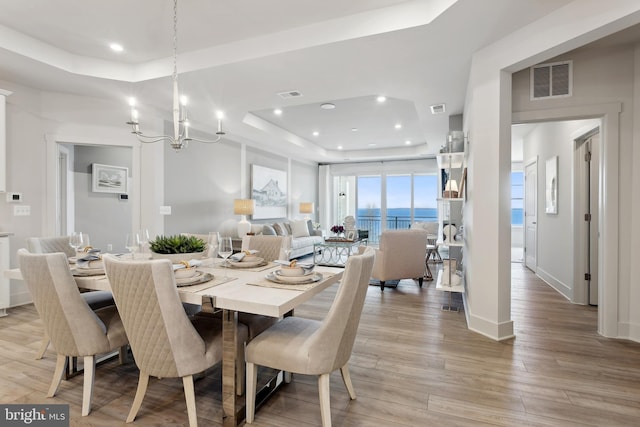 dining space with a tray ceiling, a water view, light hardwood / wood-style floors, and a notable chandelier