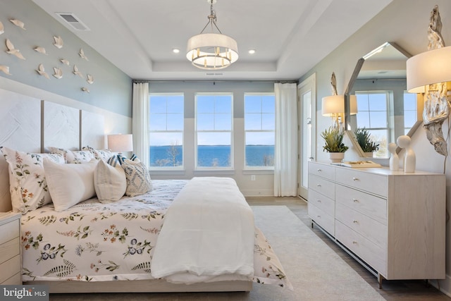 bedroom featuring a water view, wood-type flooring, and a tray ceiling