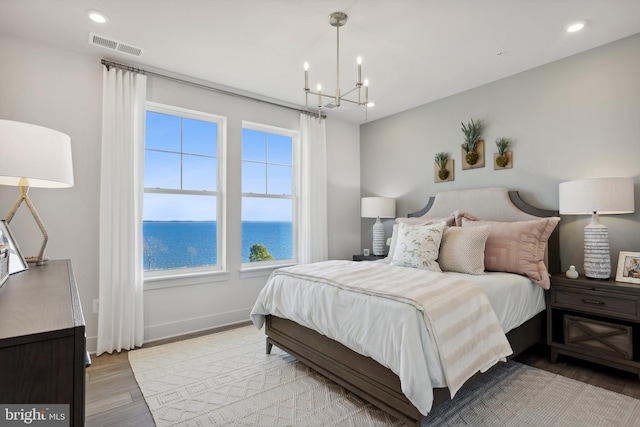 bedroom featuring an inviting chandelier, a water view, and light hardwood / wood-style flooring