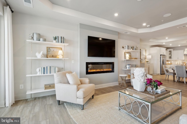 living room with light hardwood / wood-style floors and a raised ceiling