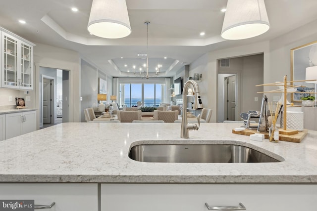 kitchen featuring light stone countertops, a tray ceiling, sink, white cabinets, and hanging light fixtures