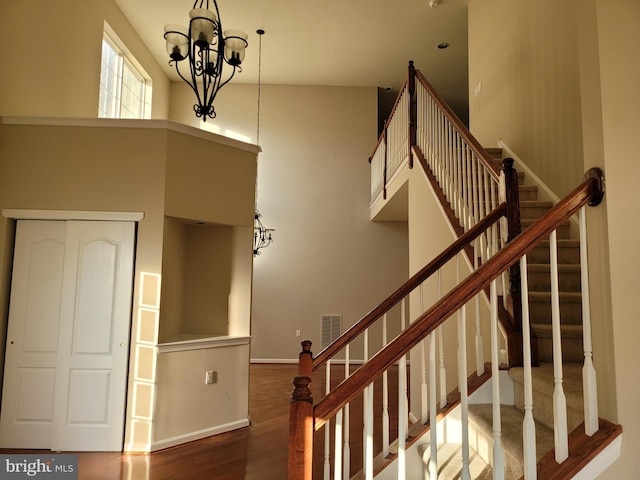 staircase with a notable chandelier, wood-type flooring, and a towering ceiling