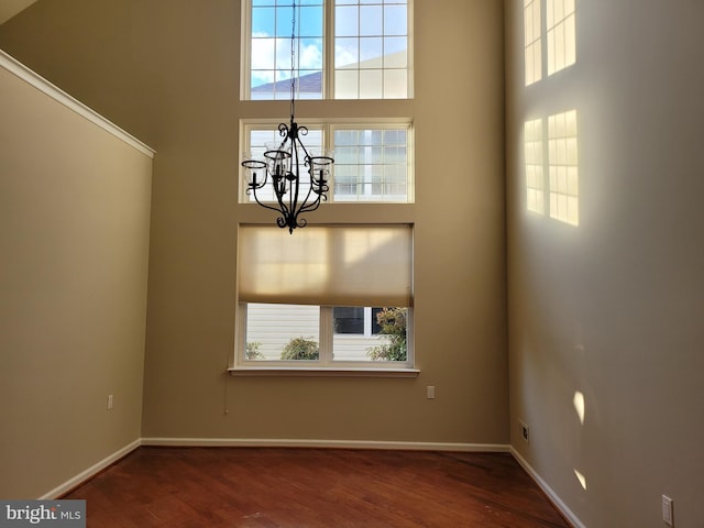 unfurnished dining area with a chandelier, a high ceiling, and hardwood / wood-style flooring