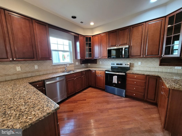 kitchen featuring appliances with stainless steel finishes, dark hardwood / wood-style flooring, tasteful backsplash, light stone counters, and sink