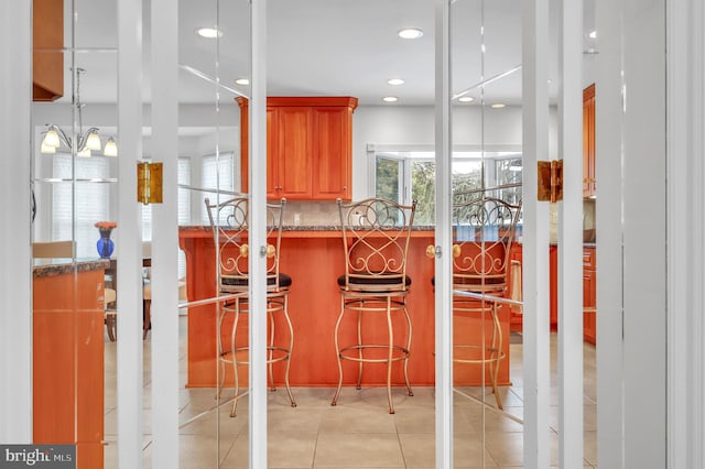 interior space featuring decorative backsplash, a breakfast bar, light tile patterned floors, stone countertops, and a chandelier