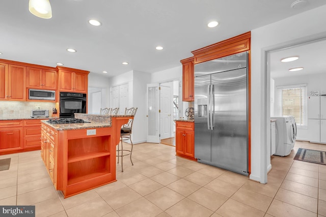 kitchen featuring washing machine and clothes dryer, backsplash, built in appliances, a breakfast bar area, and a kitchen island