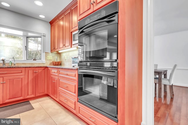 kitchen featuring light stone countertops, built in microwave, sink, black double oven, and decorative backsplash