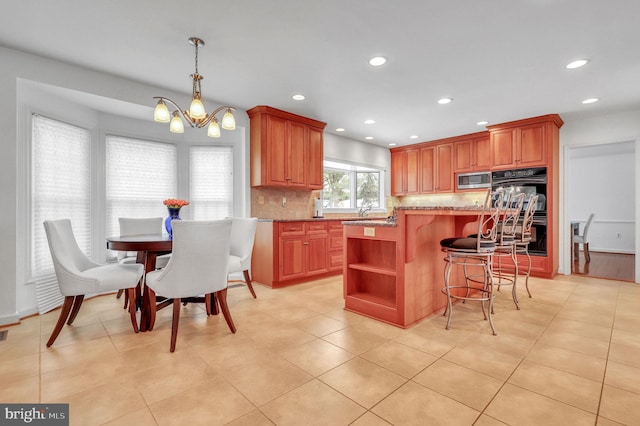 kitchen with an inviting chandelier, hanging light fixtures, light stone countertops, tasteful backsplash, and a kitchen island