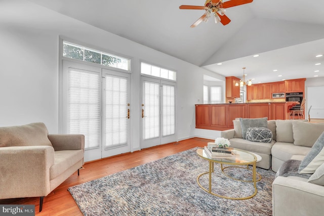 living room featuring ceiling fan with notable chandelier, light hardwood / wood-style floors, and vaulted ceiling