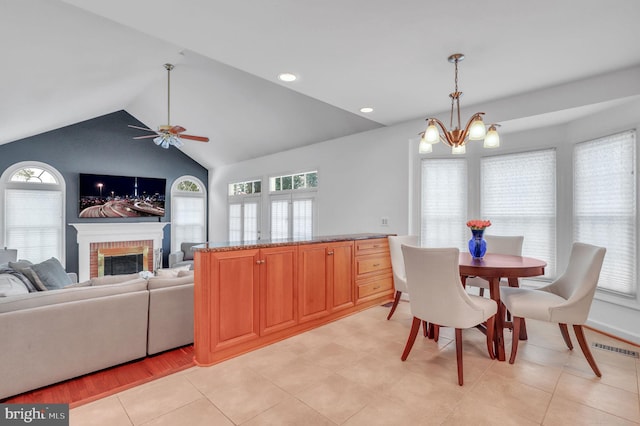 dining area featuring a fireplace, light tile patterned floors, ceiling fan with notable chandelier, and lofted ceiling