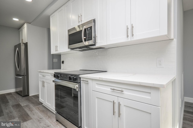 kitchen featuring white cabinets, hardwood / wood-style flooring, decorative backsplash, light stone countertops, and appliances with stainless steel finishes