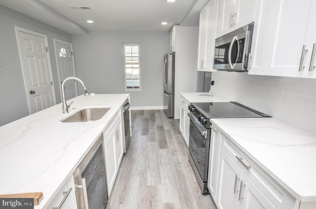 kitchen featuring white cabinets, sink, light stone countertops, appliances with stainless steel finishes, and light hardwood / wood-style floors