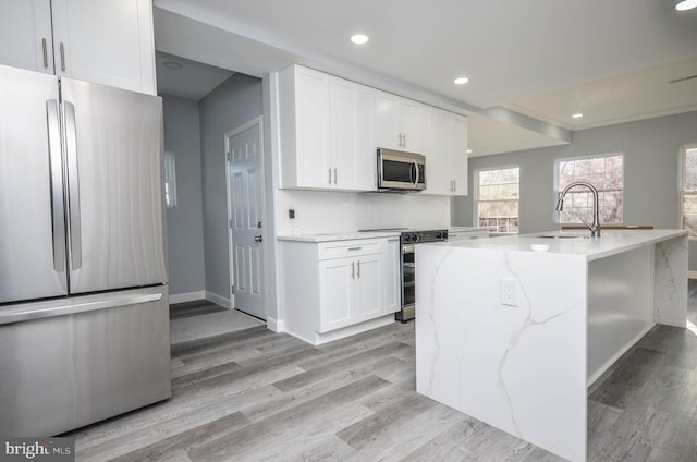 kitchen featuring sink, light stone countertops, an island with sink, appliances with stainless steel finishes, and white cabinetry