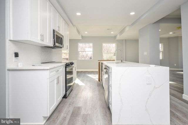 kitchen with white cabinetry, sink, light stone countertops, an island with sink, and appliances with stainless steel finishes