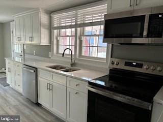 kitchen with appliances with stainless steel finishes, light hardwood / wood-style flooring, white cabinetry, and sink