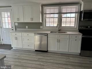 kitchen with appliances with stainless steel finishes, light wood-type flooring, white cabinetry, and sink