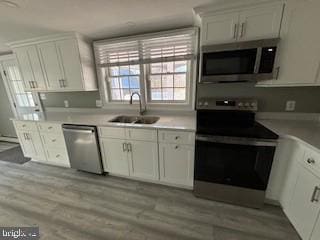 kitchen with white cabinets, appliances with stainless steel finishes, light hardwood / wood-style flooring, and sink