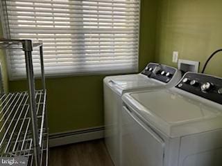 clothes washing area featuring washing machine and clothes dryer, a healthy amount of sunlight, a baseboard radiator, and wood-type flooring