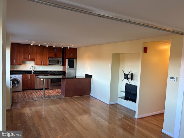 kitchen with sink, light hardwood / wood-style flooring, track lighting, washer / dryer, and appliances with stainless steel finishes