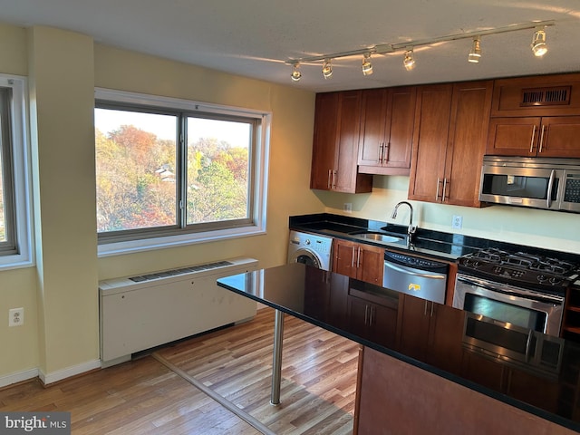 kitchen featuring radiator, sink, stainless steel appliances, washer / clothes dryer, and light wood-type flooring