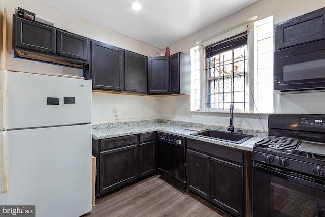 kitchen with light stone counters, sink, black appliances, and light hardwood / wood-style flooring