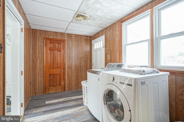 washroom with washing machine and clothes dryer, wood walls, plenty of natural light, and dark wood-type flooring