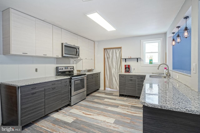 kitchen with light stone counters, stainless steel appliances, sink, pendant lighting, and light hardwood / wood-style floors