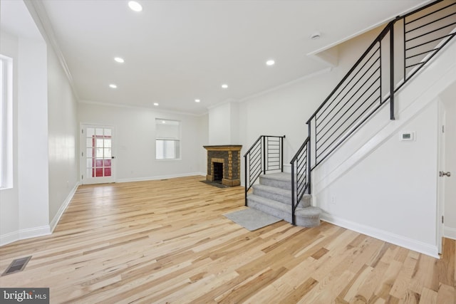 unfurnished living room featuring a brick fireplace, crown molding, and light hardwood / wood-style flooring