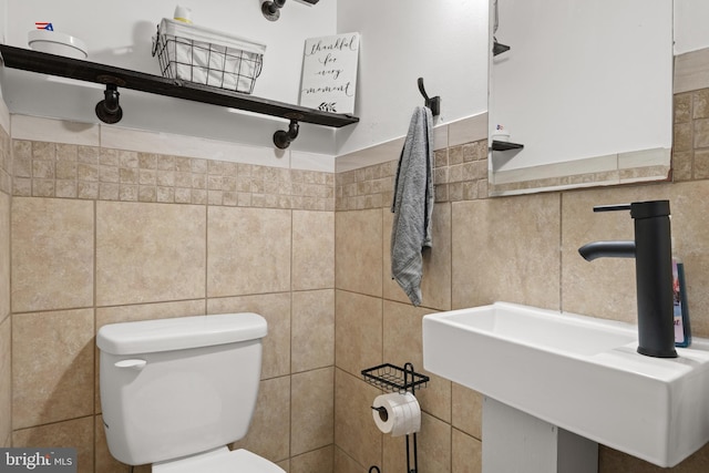 bathroom with toilet, sink, and tile walls