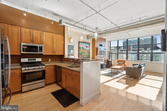 kitchen with light stone countertops, sink, kitchen peninsula, decorative light fixtures, and appliances with stainless steel finishes