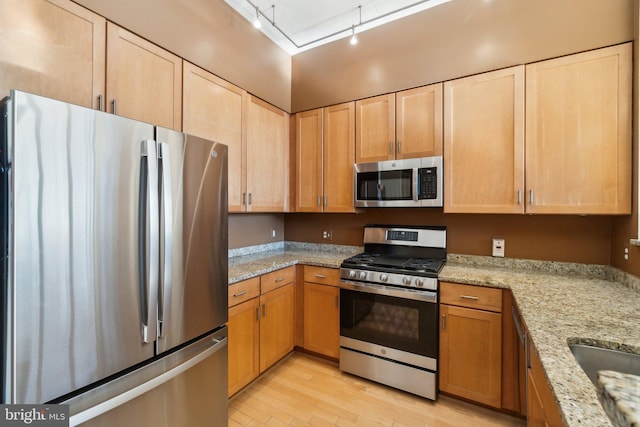 kitchen featuring light stone counters, light hardwood / wood-style flooring, track lighting, and appliances with stainless steel finishes