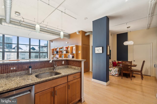 kitchen with light stone counters, sink, stainless steel dishwasher, and decorative light fixtures