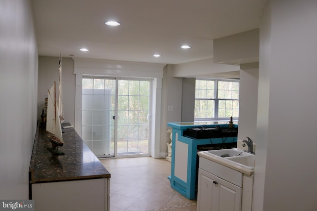 kitchen with white cabinetry, sink, light tile patterned floors, and dark stone counters